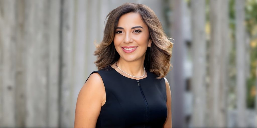 Nayla Chebli, founder of iMasterLanguages, smiling confidently in a professional black dress, with a blurred background.