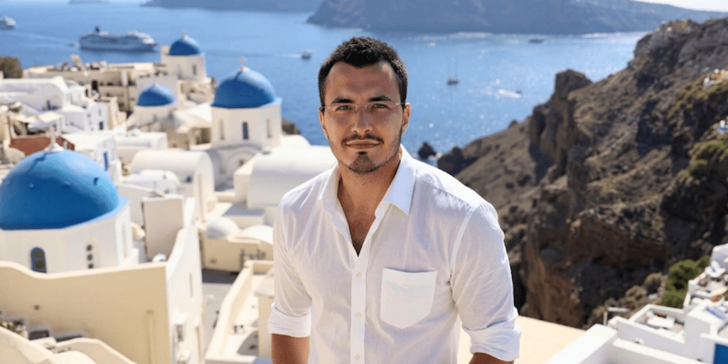 Man posing in Santorini with blue domes and sea, showcasing luxury travel lifestyle branding.