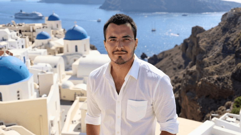 Man posing in Santorini with blue domes and sea, showcasing luxury travel lifestyle branding.