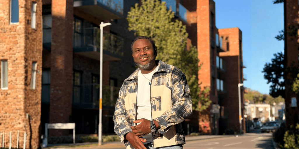 Kenny Ojo smiling outdoors in an urban neighborhood, reflecting confidence, community, and authentic storytelling.