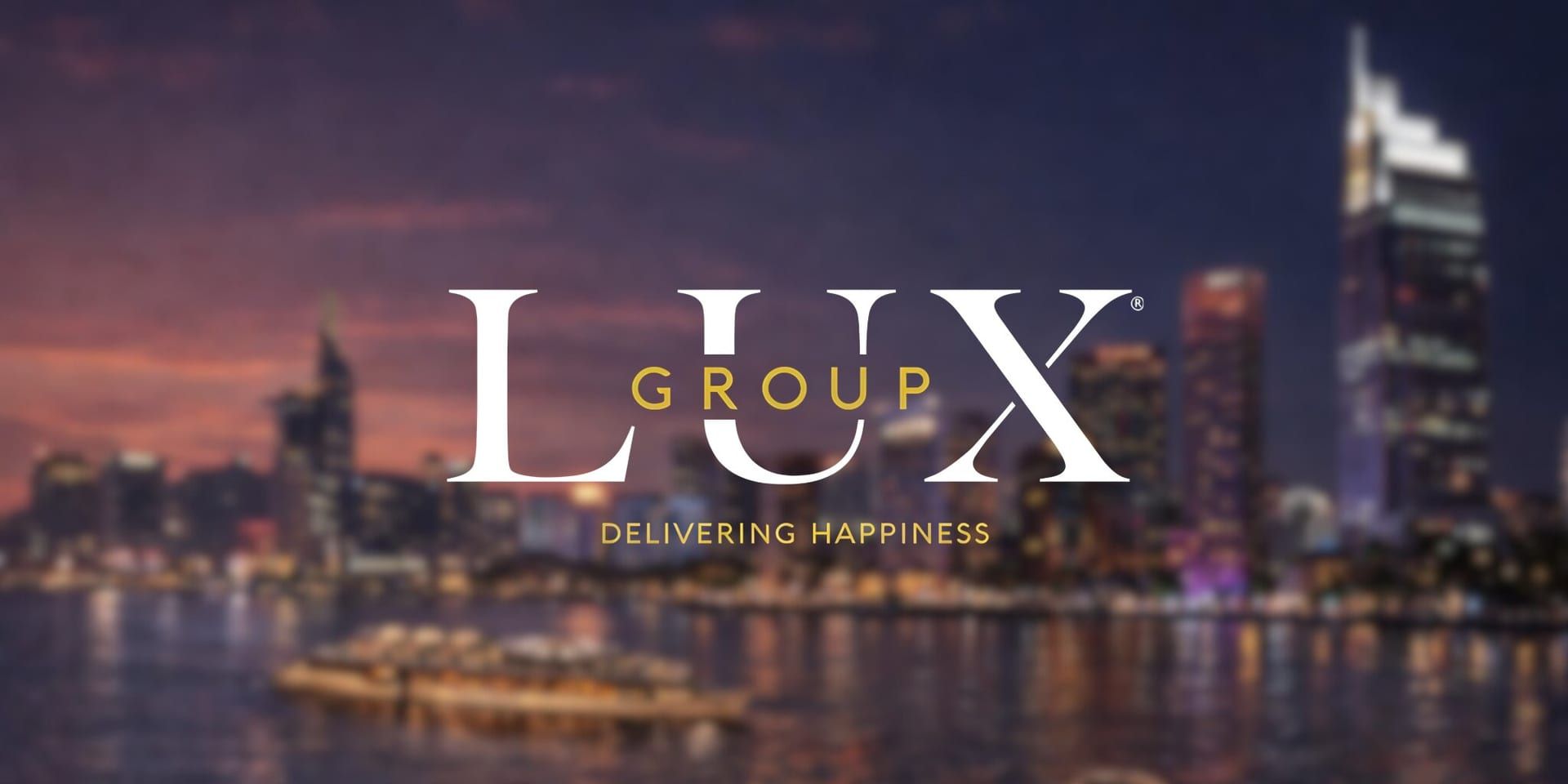 "Lux Group logo overlays a blurry city skyline at dusk, with soft lights reflecting on the water. The tagline reads 'Delivering Happiness.'"
