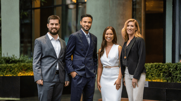 Four professionals in business attire pose outside a modern office building, representing Medallion Investments' team.