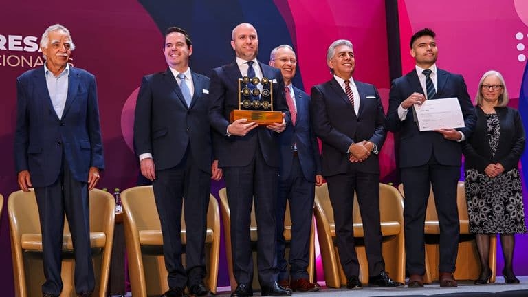 A group of people standing together on stage at an awards ceremony, with one person holding a trophy while others are smiling.