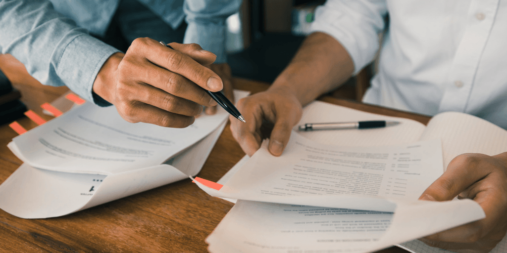 Two people reviewing documents, pointing to highlighted sections with pens.