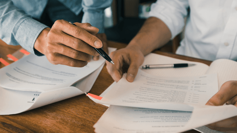 Two people reviewing documents, pointing to highlighted sections with pens.