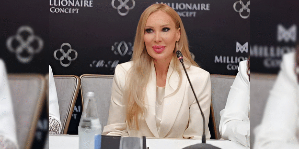 Laura Svag speaking at a press event, wearing a white suit with a microphone in front of her.