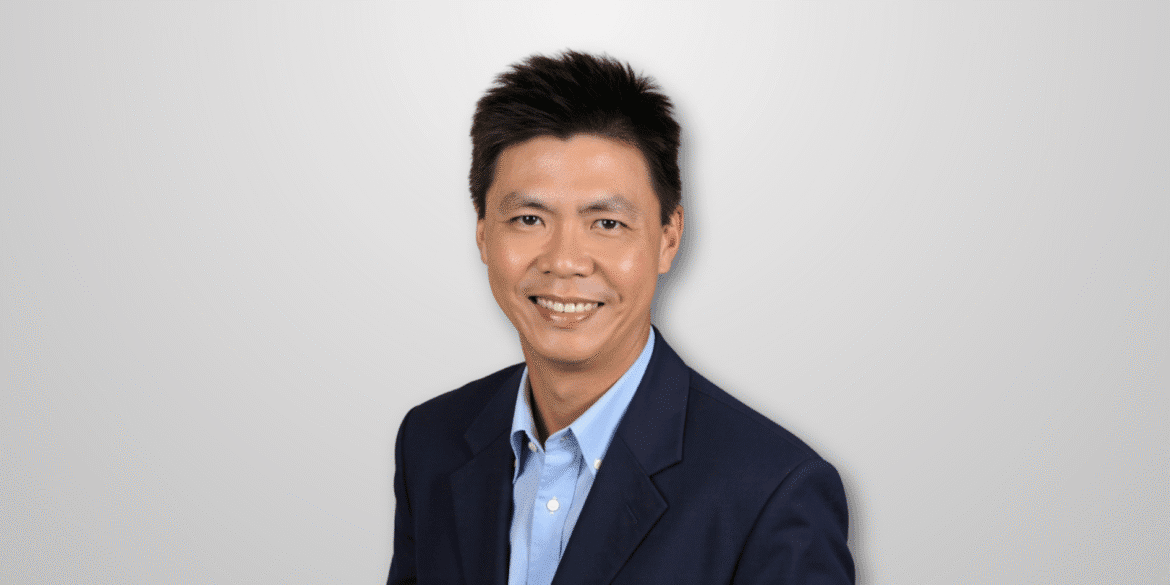 Headshot of a smiling man in a blue blazer, with short hair and a professional demeanor, set against a white background.