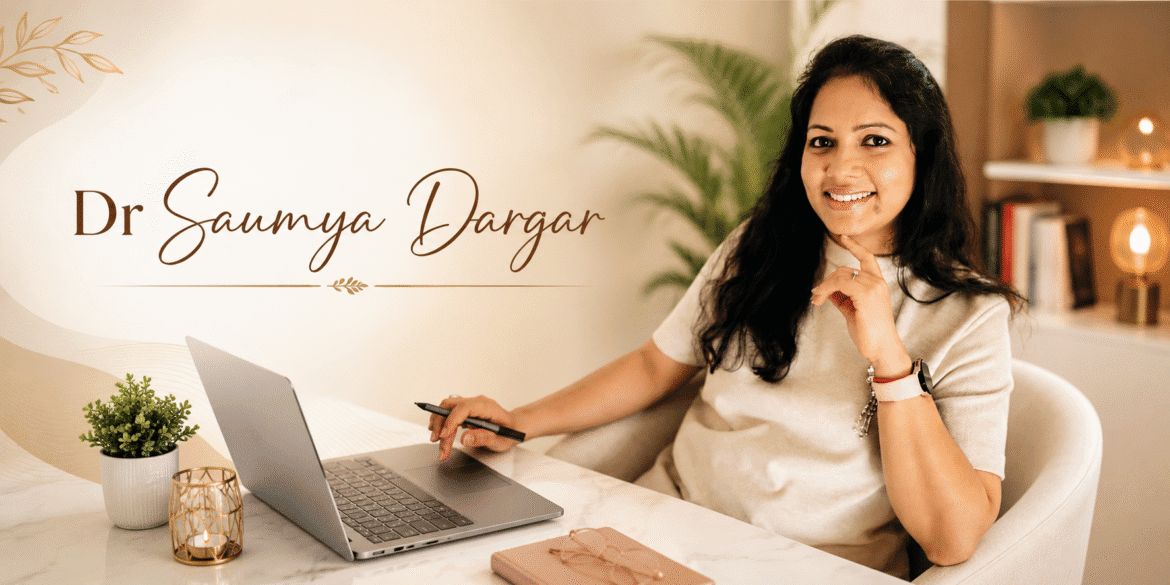 Dr. Saumya Dargar smiling at a desk with laptop in a warm office, professional personal branding portrait.