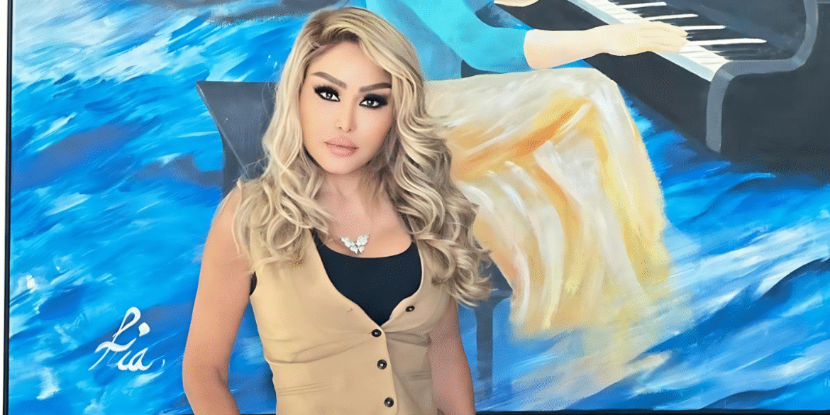 "Portrait of a woman with blonde hair standing in front of a colorful abstract painting, featuring a piano and blue tones, wearing a beige vest and a statement necklace. The painting is signed 'Lia' in white."