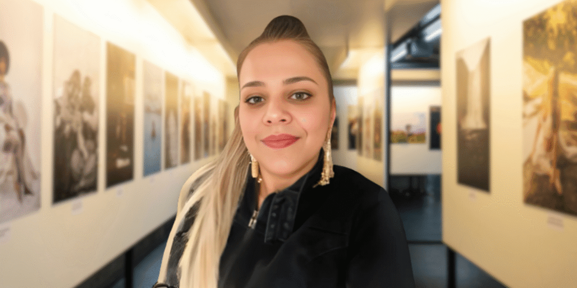 Woman smiling in an art gallery hallway lined with large, framed photographs on both walls.