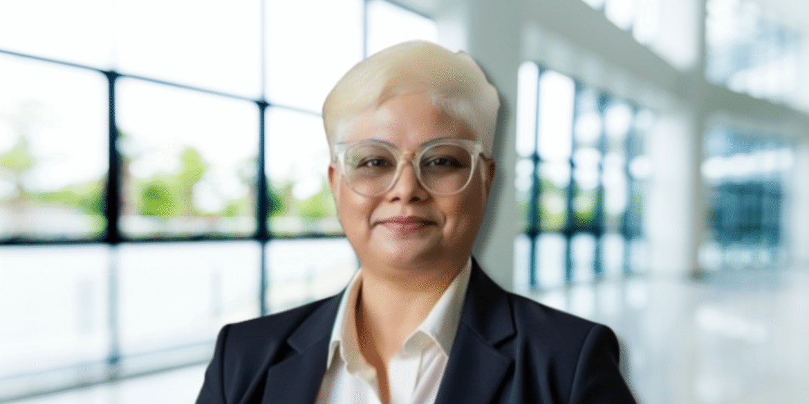 Dr. Alice Preetha in a business suit, smiling confidently inside a bright, modern office building.