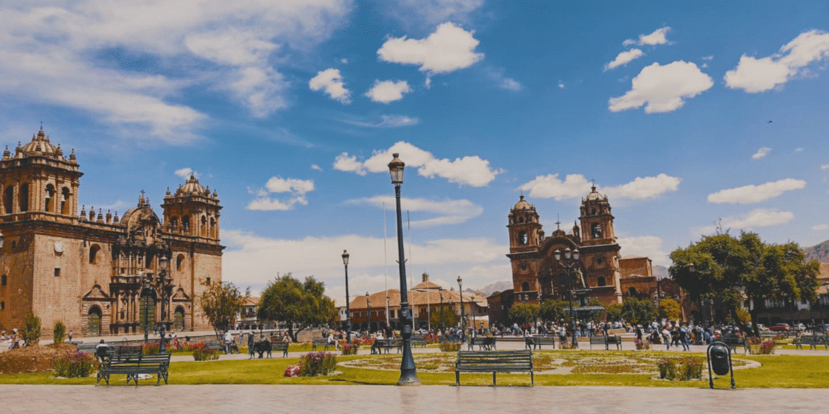 Plaza de Armas in Cusco, Peru, with historic churches and vibrant crowds under a bright blue sky.