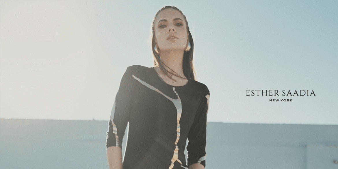 Elegant woman wearing a black modest dress with metallic accents, photographed outdoors in soft natural sunlight.