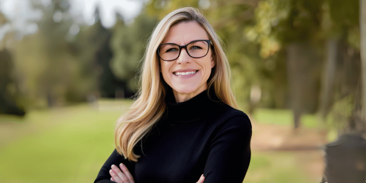 Smiling woman in black sweater and glasses standing outdoors, representing Elisha Meek’s journey from burnout to purpose.