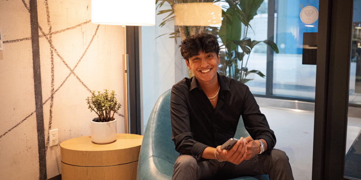 Devan Tiankee, founder of Daygency, smiles while seated in a modern office space, holding a phone.