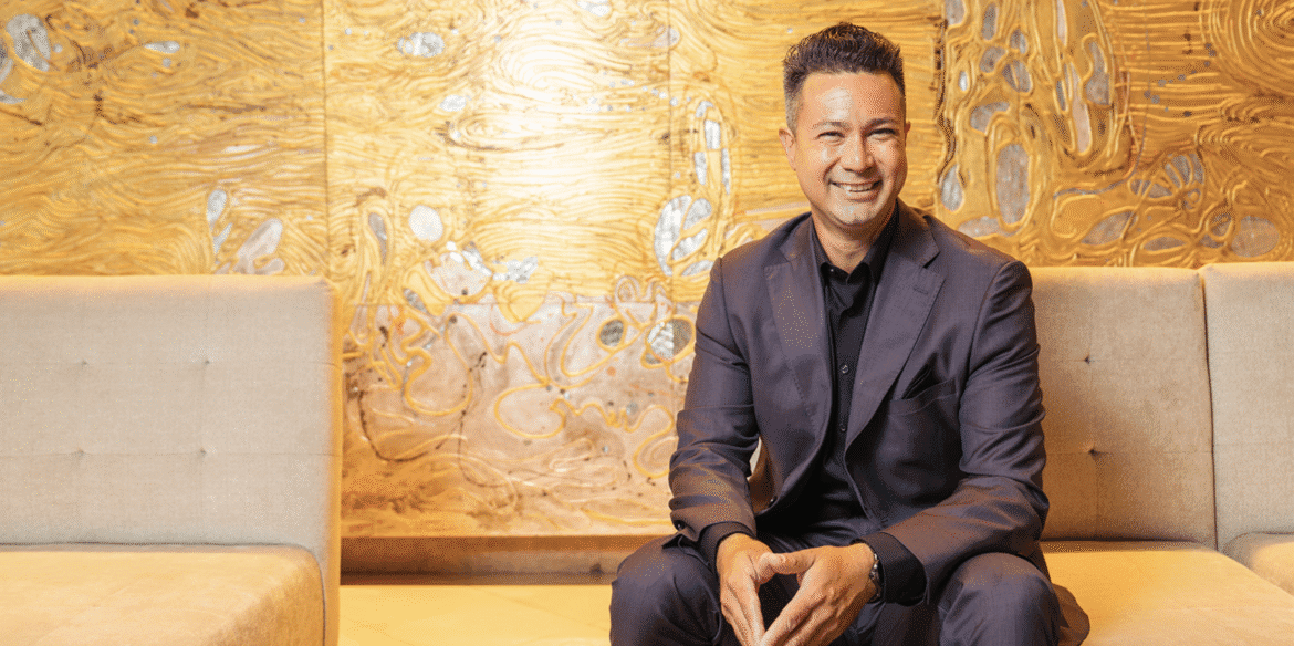 Christopher Robin Gallego, founder of Firewise Fences, stands before a fire-resistant fence, symbolizing his shift from filmmaker to entrepreneur focused on wildfire resilience.