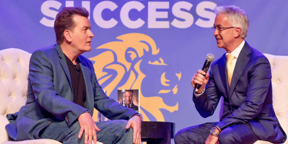 Craig Carr speaks on stage with another man during a business success event promoting psychology-based wealth and sales strategies.