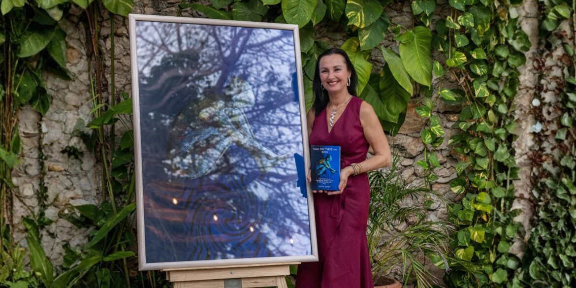 The image features Dra. Katha Jones standing beside a framed artwork, holding her book "Think Outside the Box."