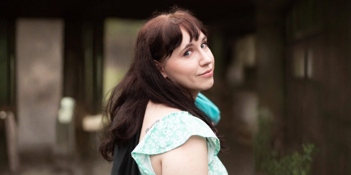 A woman with long brown hair wearing a blue scarf, looking thoughtfully into the distance.