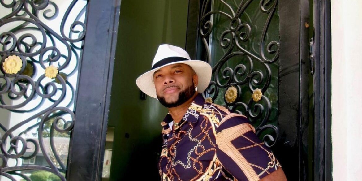 Enoch Duplechan standing confidently in a stylish shirt and hat, symbolizing leadership grounded in faith, purpose, and people.