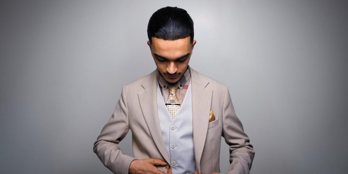 Cinen Hamila, founder of Magik Management, in a beige suit with geometric tie and golden pocket square, focused.