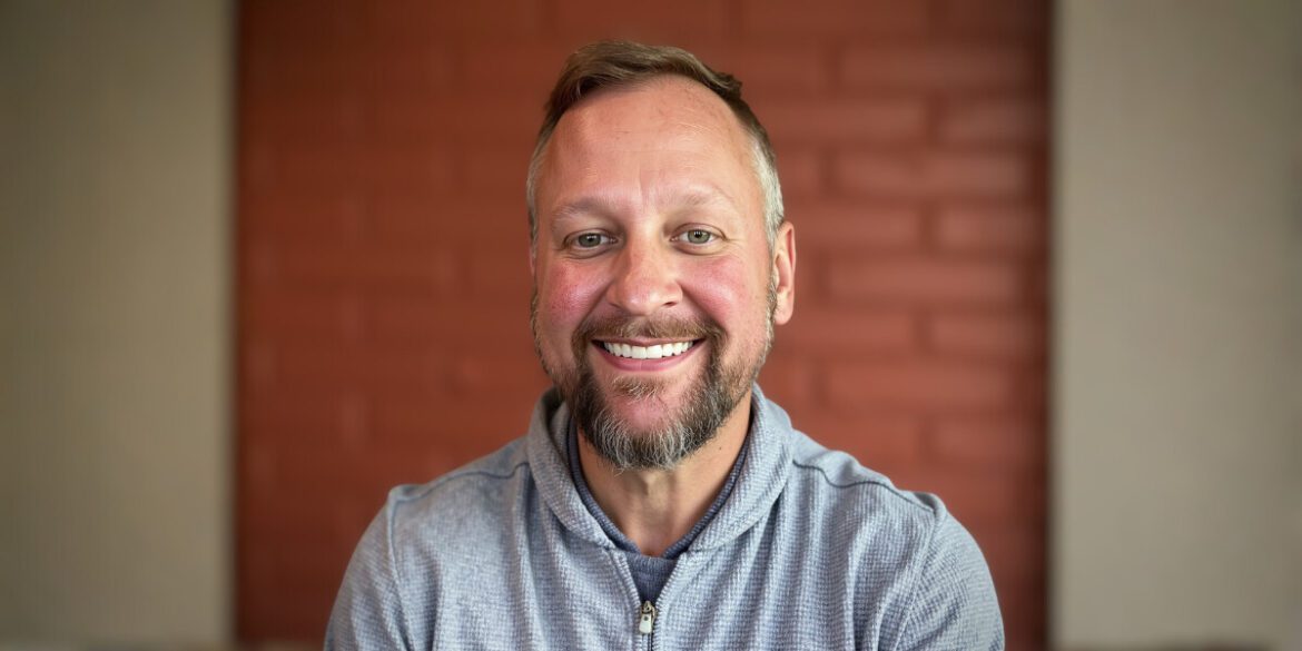 Mike Snellenberger, the founder of The Fractional CMO Team, smiling confidently with a brick wall background.