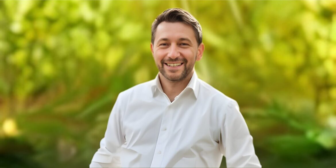 A smiling man in a white shirt stands in front of a vibrant green background, embodying positivity and confidence.