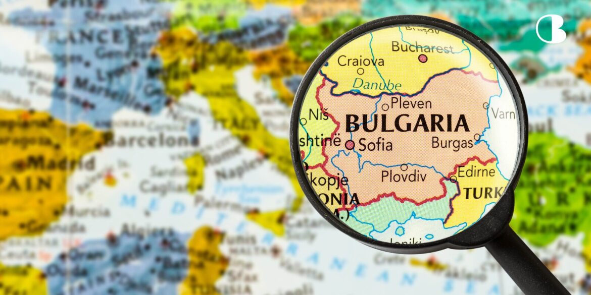 A magnifying glass highlights Bulgaria on a colorful map of Europe, showing nearby countries and the Black Sea. The focus conveys exploration and detail.