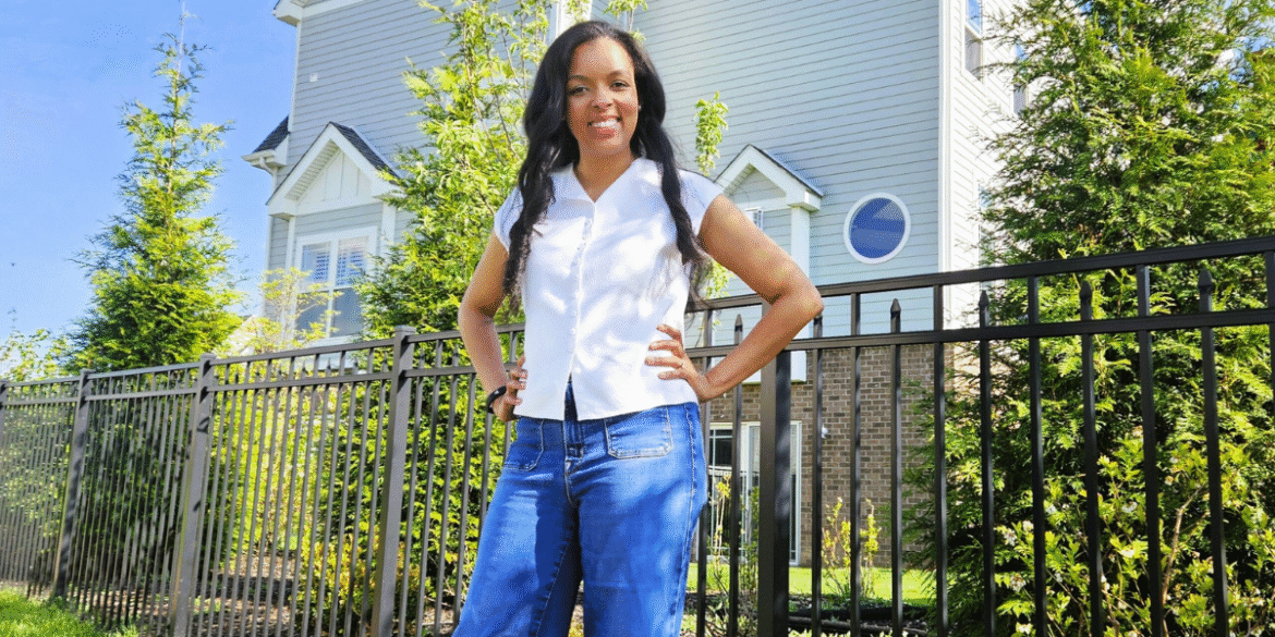 Woman standing confidently in front of a residential property and community fence.