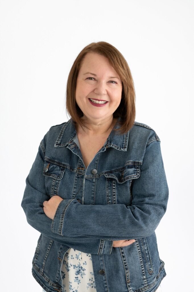 Smiling author Christina Bedal wearing a denim jacket with arms crossed against a white background.