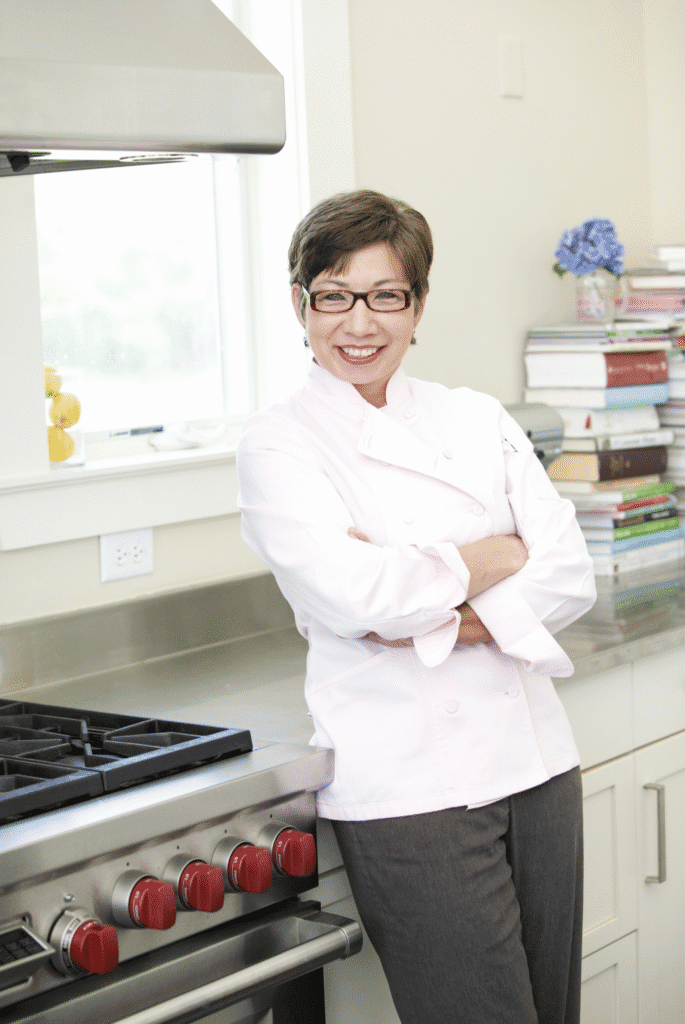 Angela McCrovitz smiling in a professional kitchen wearing a chef's coat.