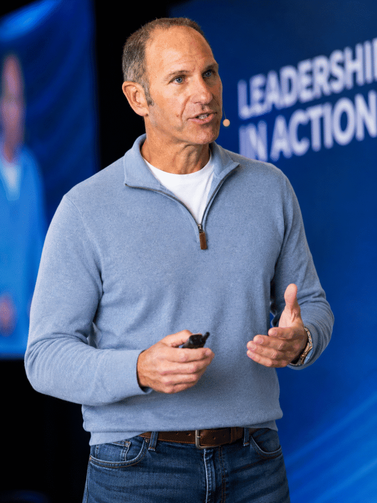 Dan Manginelli speaking on leadership and mortgage coaching at a conference, wearing headset microphone and holding presentation remote.