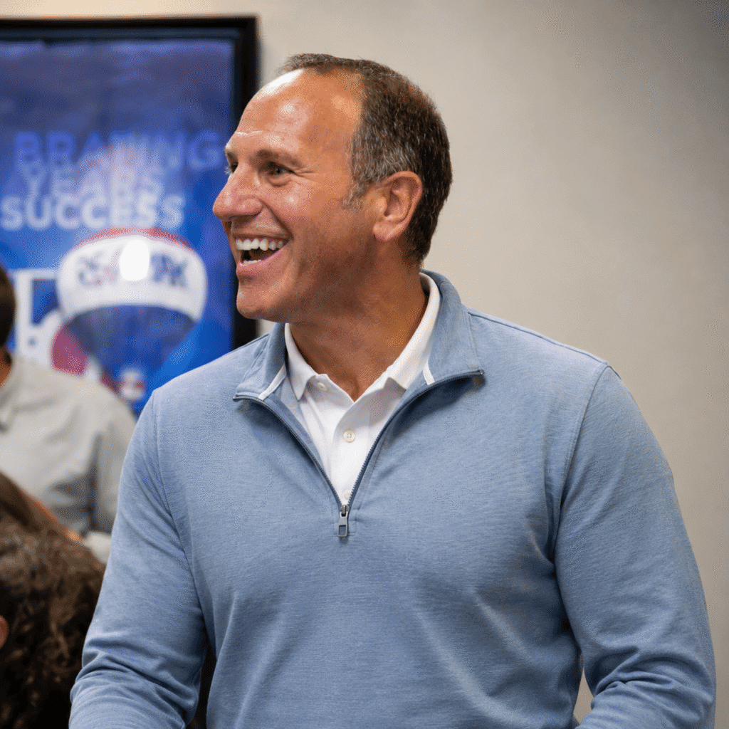 Dan Manginelli smiling while networking at a mortgage coaching event in a light blue quarter-zip sweater.