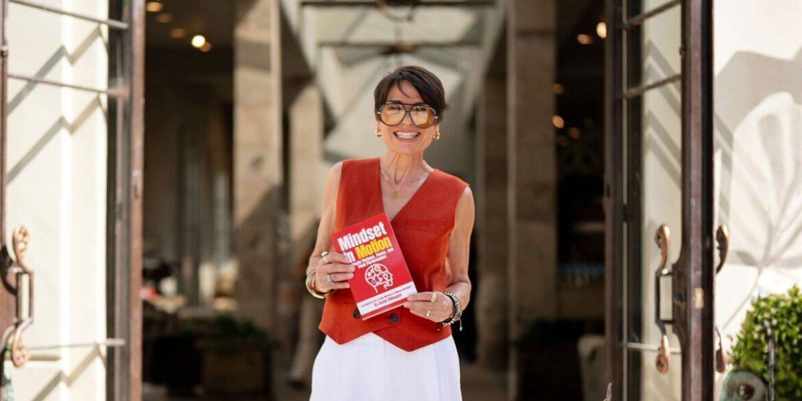 Debbi DiMaggio holds her Mindset In Motion book while standing in an open doorway.
