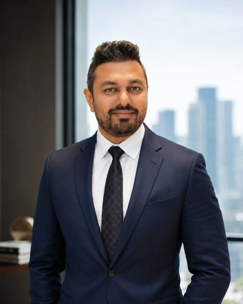 Dr. Mayur Ghule wearing a navy suit and tie in a modern office with a city skyline visible through the windows.